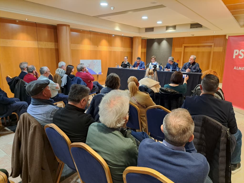 Sala de conferencias con personas sentadas y ponentes al frente. Adriana Valverde habla al público