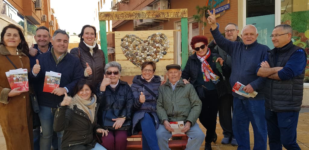 Adriana Valverde, junto a miembros de su equipo y vecinos y vecinas de El Alquián, ante una de las instalaciones de madera con motivos alusivos al amor para hacerse fotos que se repartieron por el barrio.